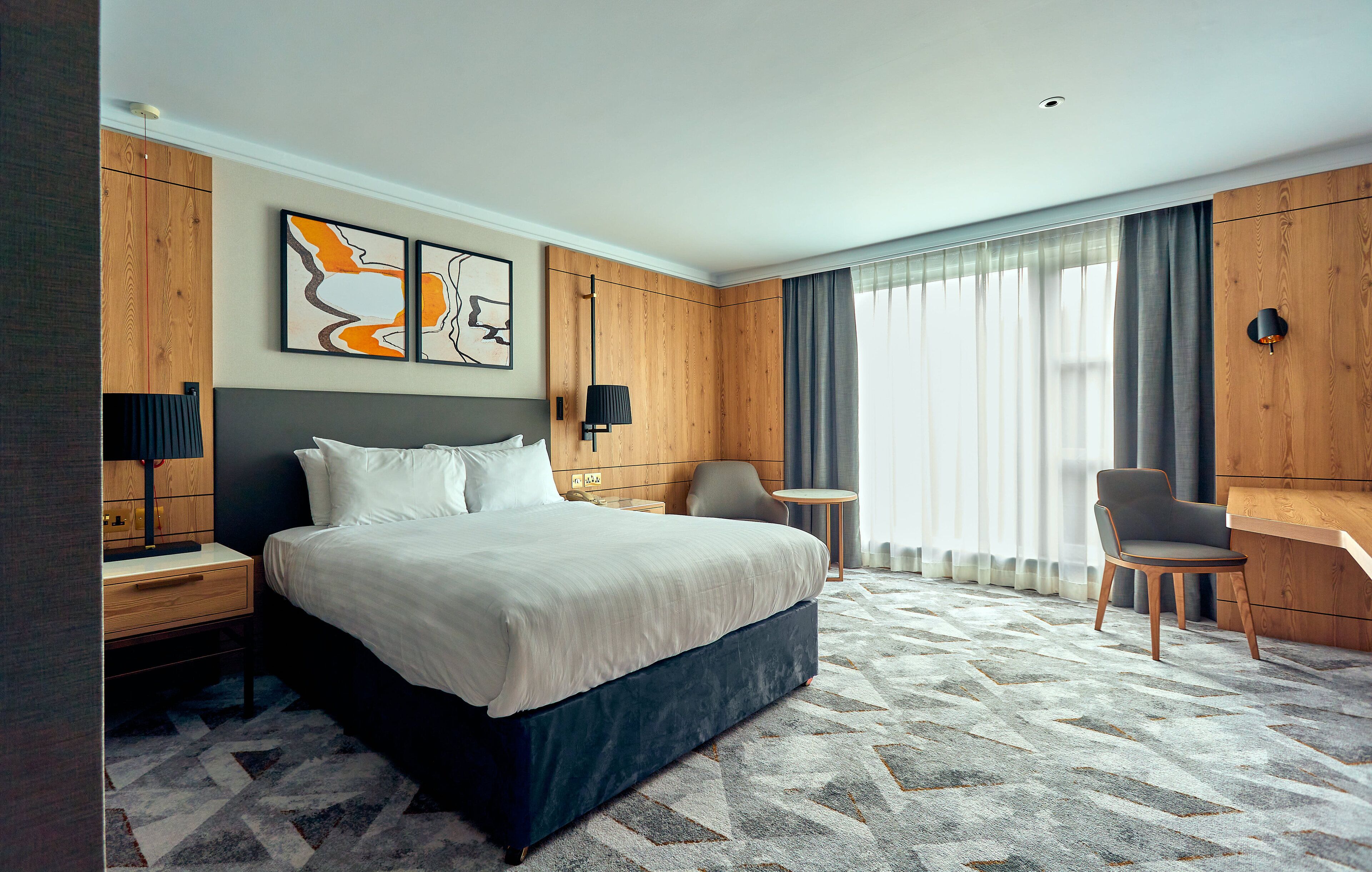 Una habitación de hotel moderna con una cama grande, un escritorio, una silla y vistas al exterior.