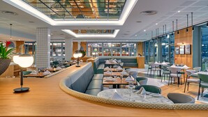 Un restaurante moderno con techo alto, paredes de vidrio y un área central con mesas y cabinas.