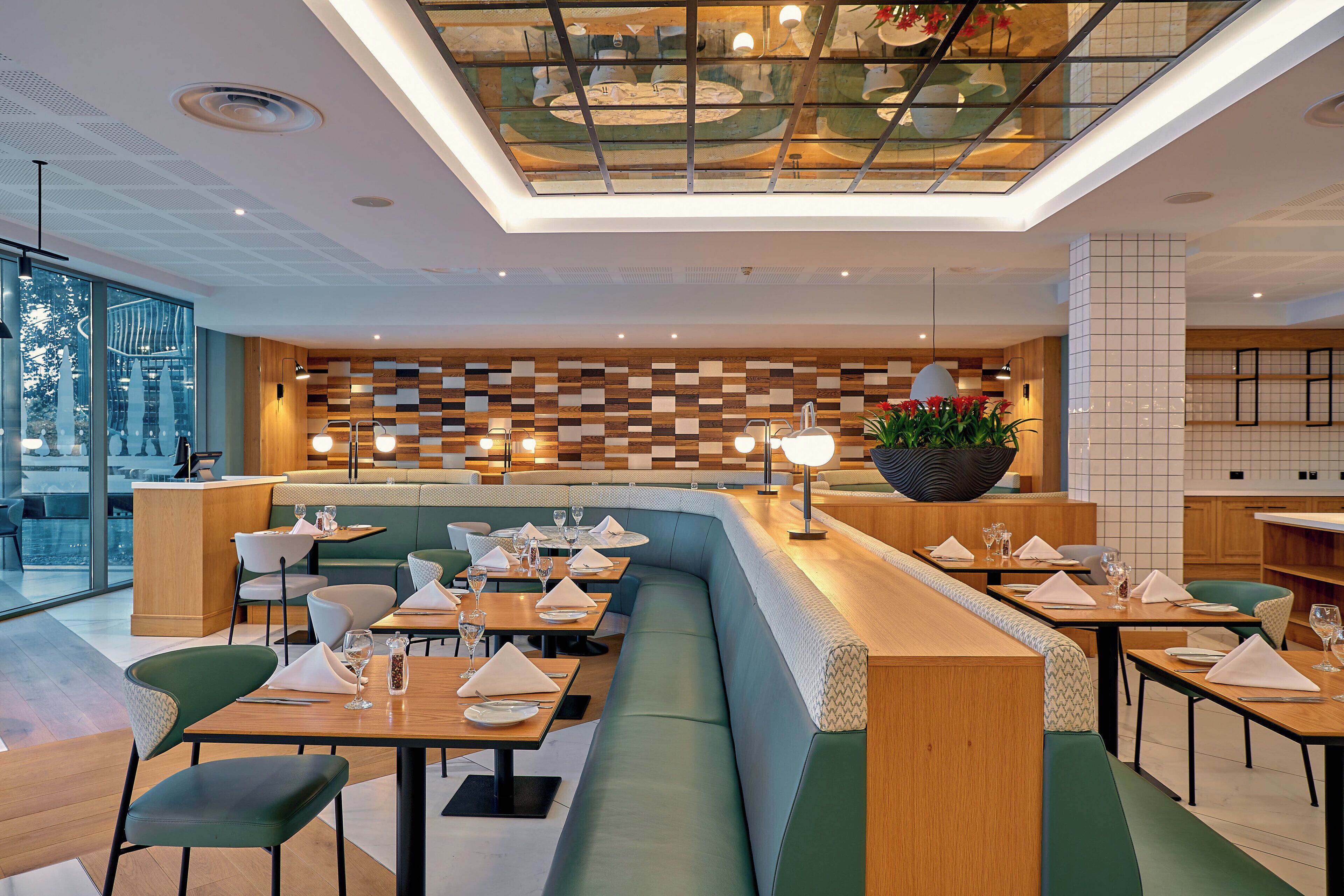 A modern restaurant interior with a high ceiling, wooden panel wall, and a mix of seating options including booths and tables.