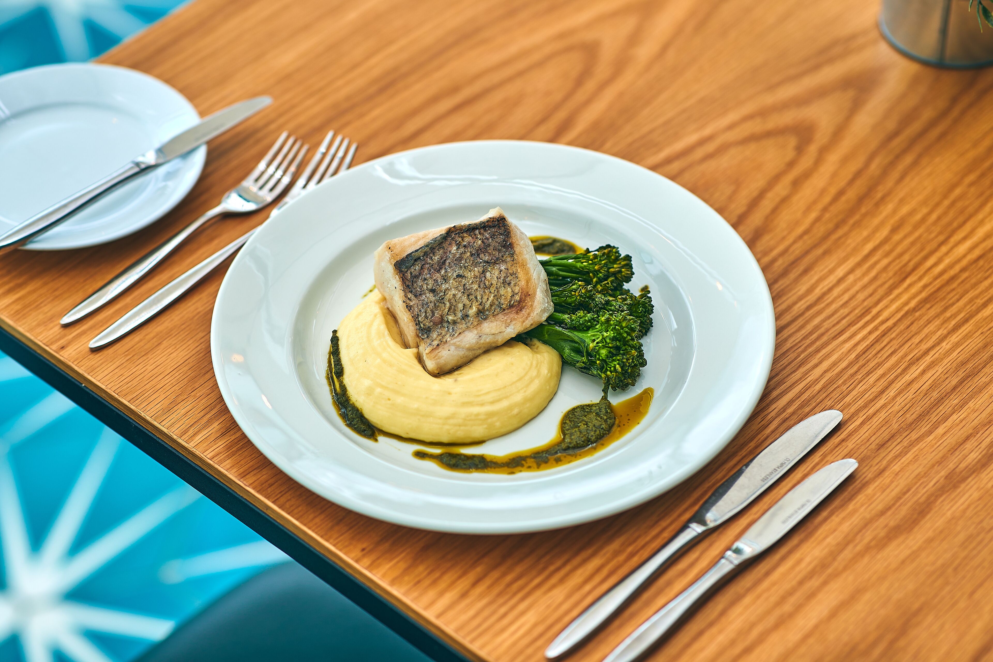A plate with a piece of fish, mashed potatoes, and broccoli on a wooden table.