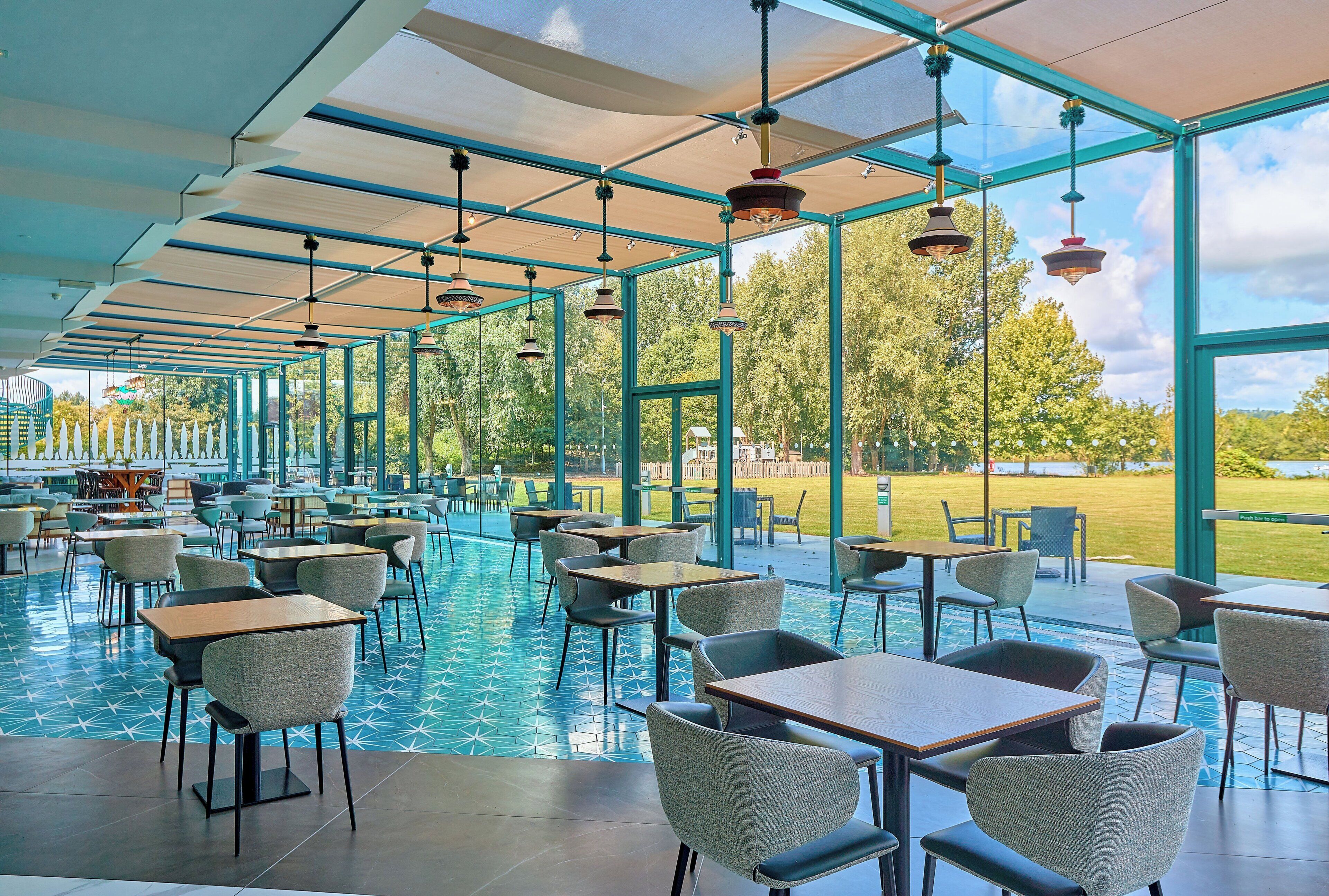 Un comedor interior con mesas y sillas, una piscina y vistas al exterior.