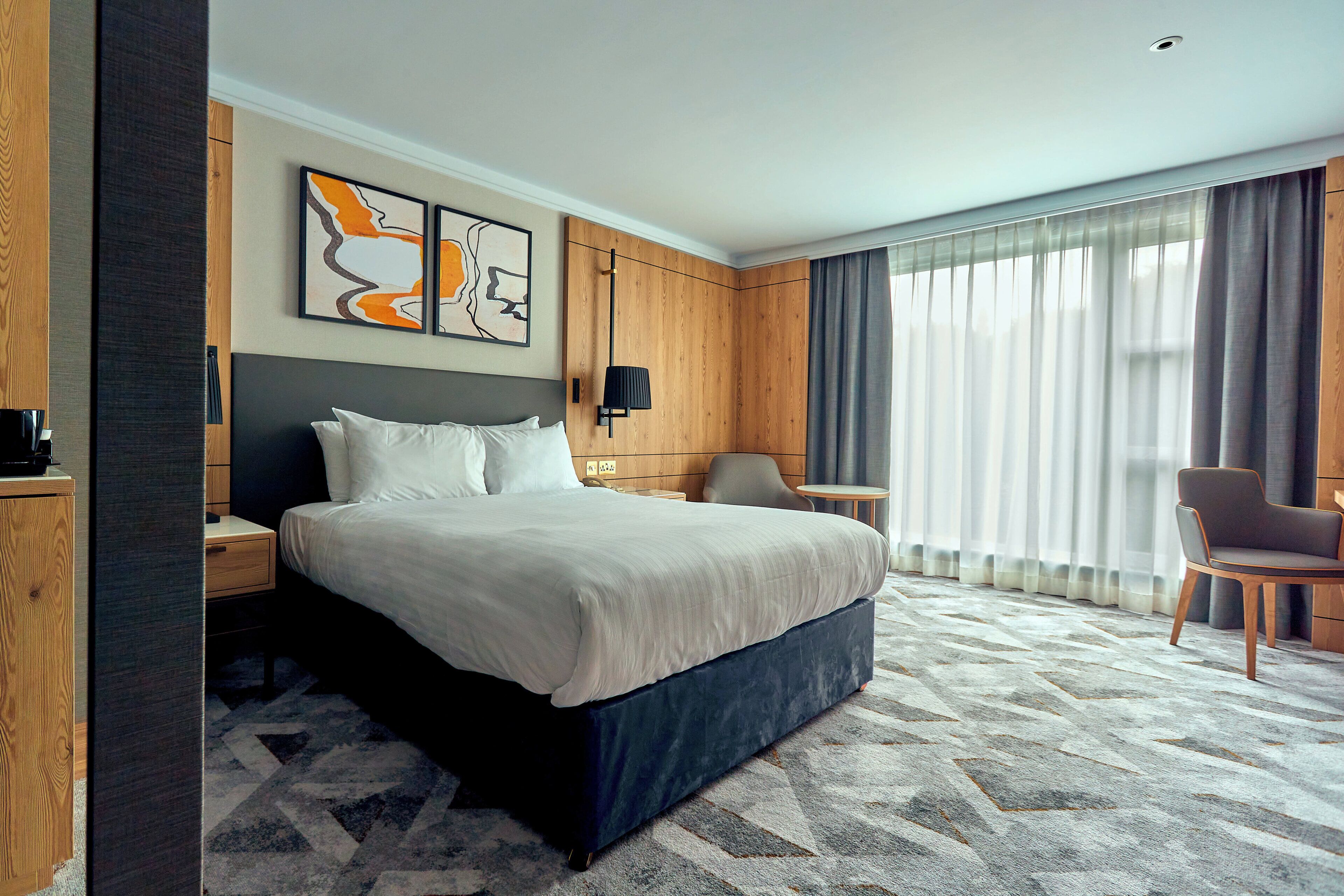 Une chambre d’hôtel avec un grand lit, un bureau, une chaise et une fenêtre avec des rideaux.