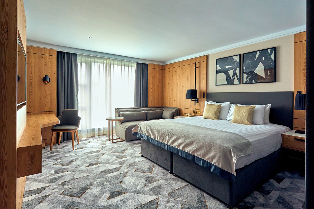 A hotel room with a large bed, a desk, a chair, and a sofa.