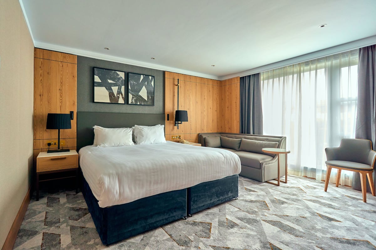 Une chambre d’hôtel moderne avec un grand lit, un canapé, un fauteuil et une petite table.