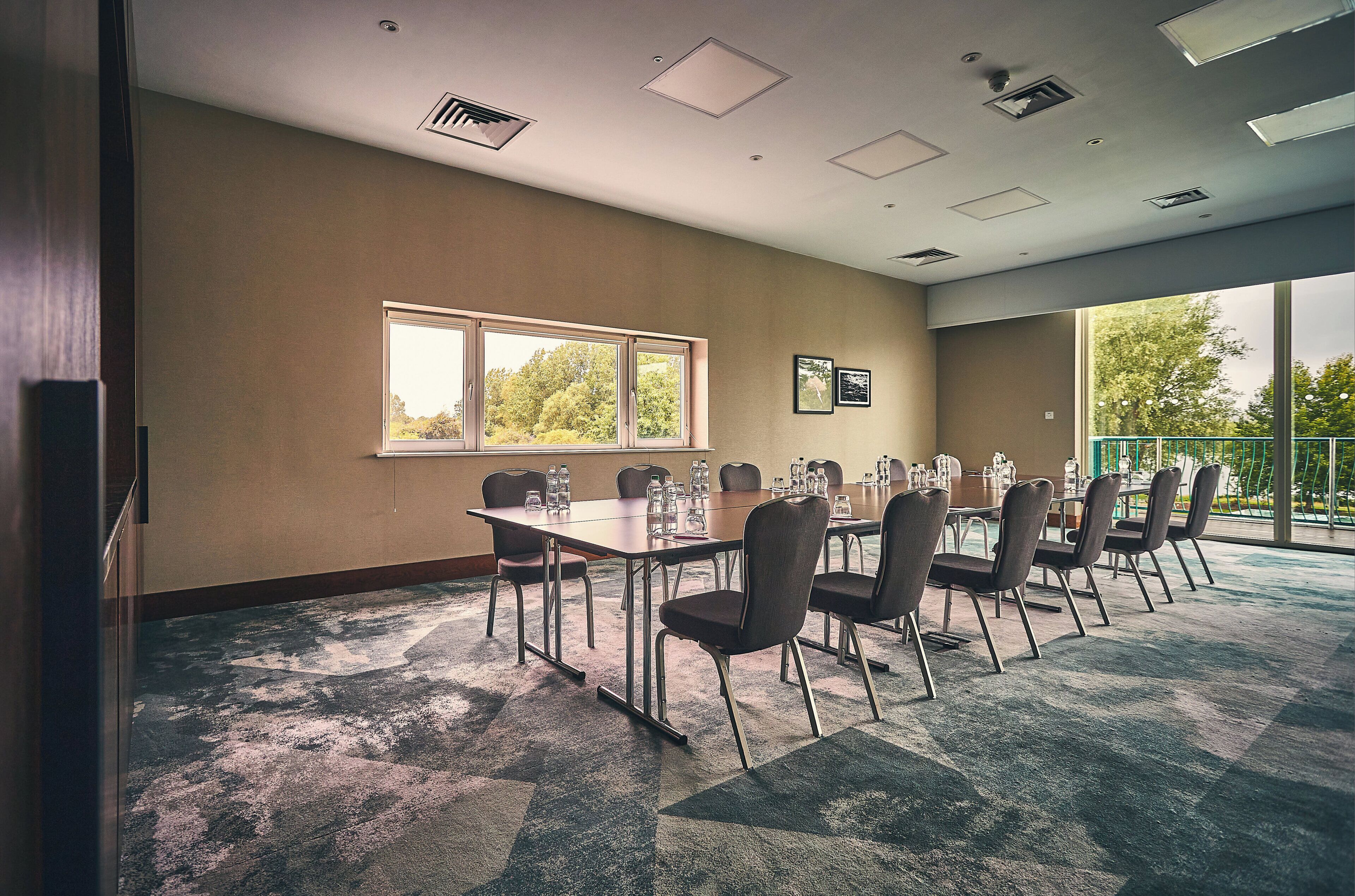 A conference room with a long table, chairs, and a large window with a view of trees.