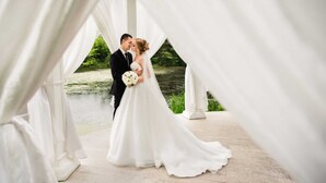 Una pareja con traje de boda bajo un dosel blanco, con un fondo natural.