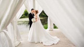 A couple in wedding attire under a white canopy with a natural background.