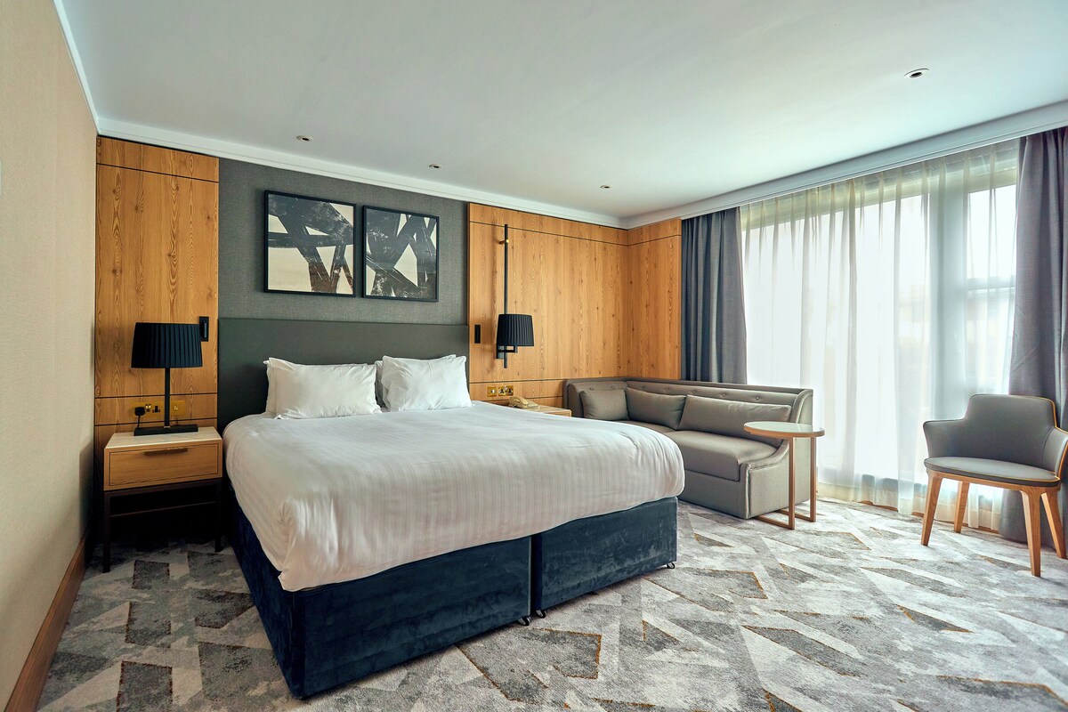 A hotel room with a large bed, a sofa, a chair, and a small table.