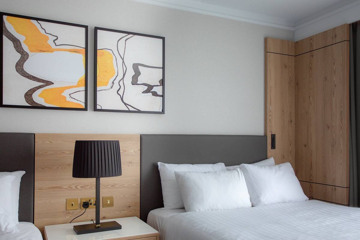 Une chambre d’hôtel avec un lit, une table de chevet, une lampe et deux tableaux abstraits accrochés au mur.
