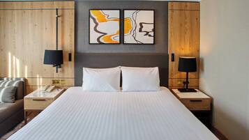A hotel room with a large bed, two bedside tables, a nightstand, a sofa, and a wall-mounted telephone.