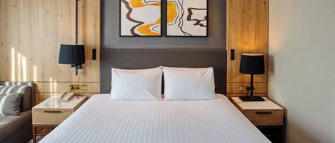 A hotel room with a large bed, two bedside tables, a nightstand, a sofa, and a wall-mounted telephone.
