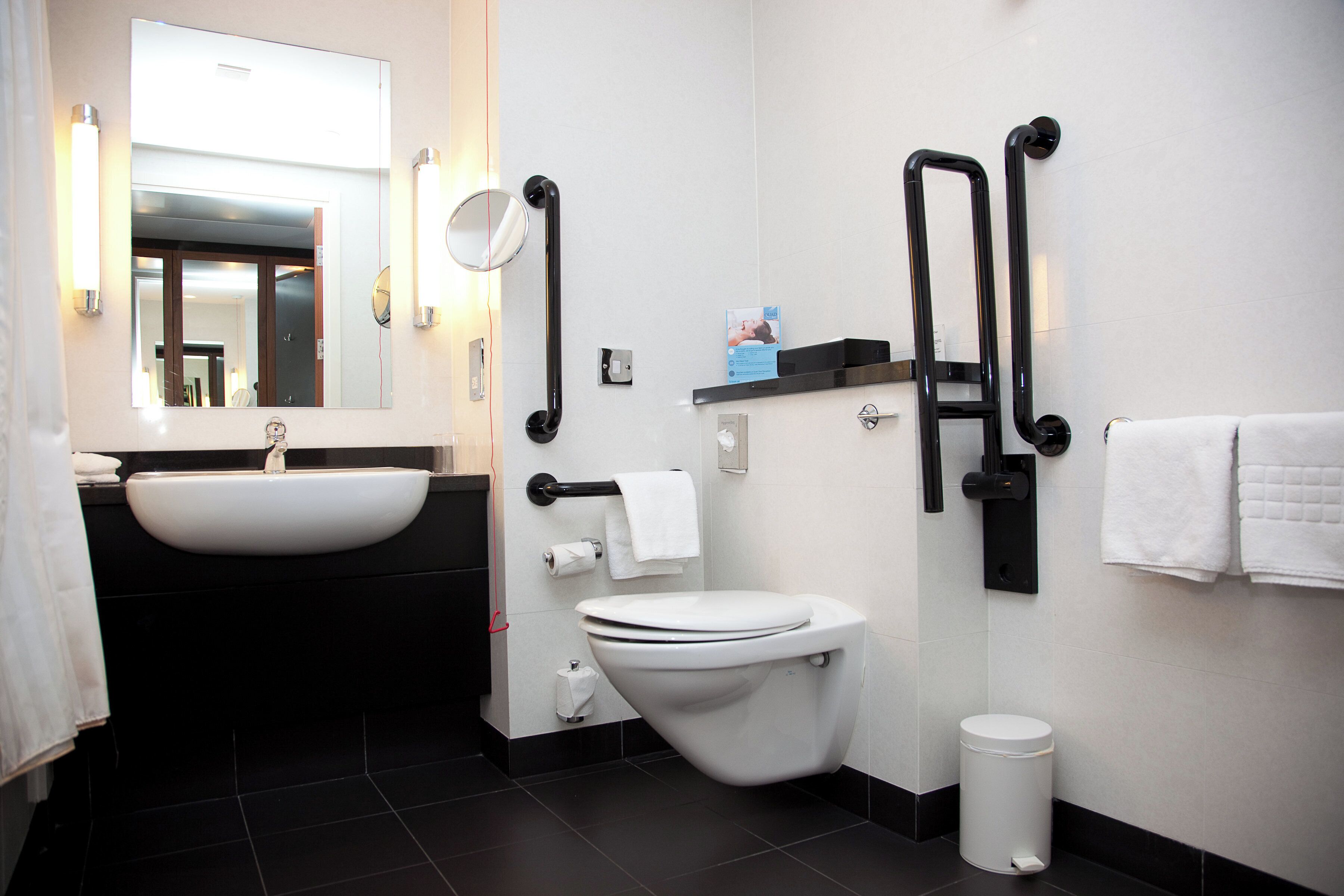 A modern bathroom with a white sink, a toilet, and a bidet. There are two towel racks and a trash bin.