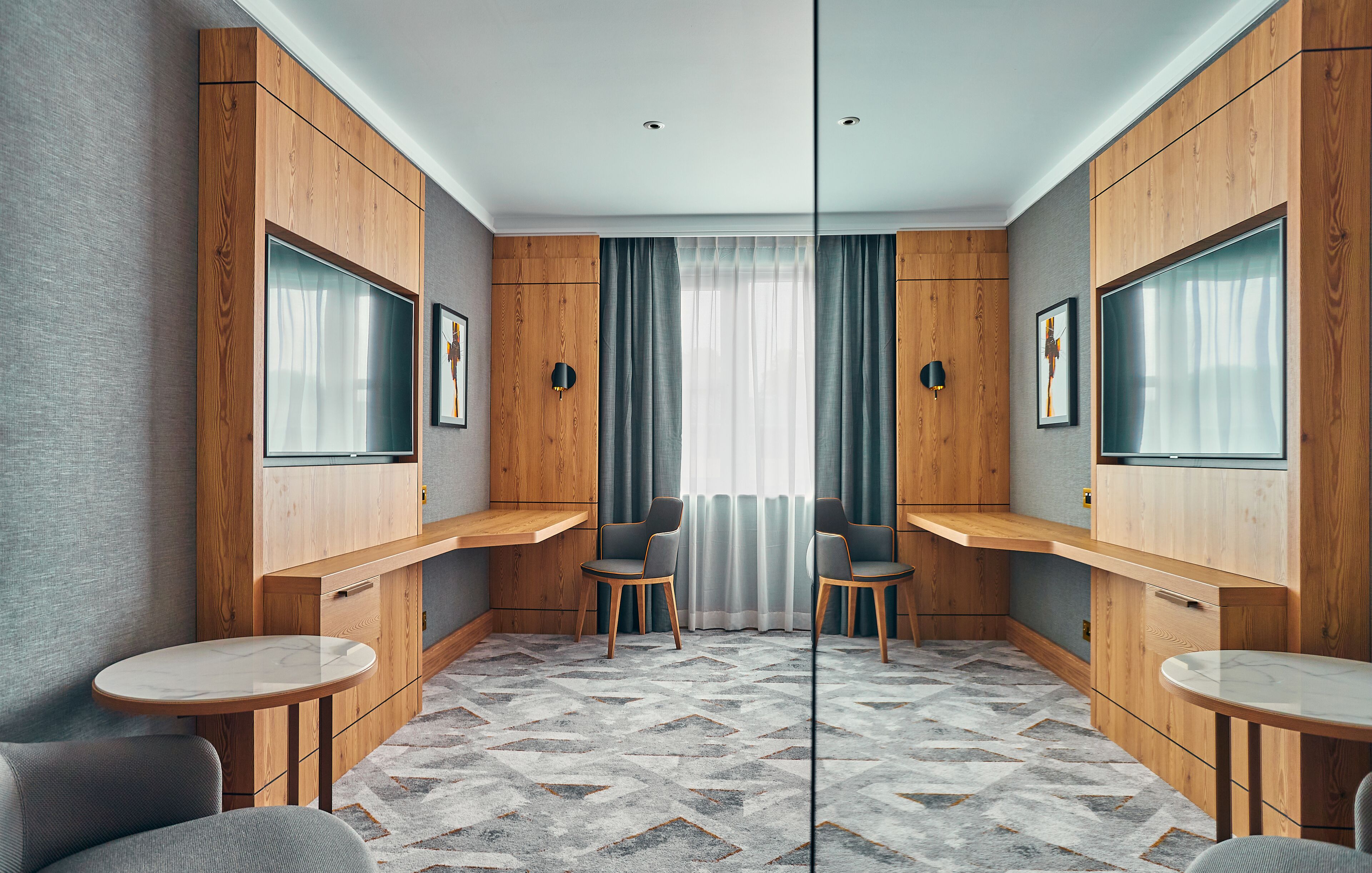 Una habitación moderna con paneles de madera, dos televisores, un ventanal con cortinas y una alfombra estampada.
