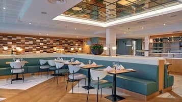 A modern restaurant with a high ceiling, wooden panel wall, and a glass ceiling. Tables and chairs are arranged for dining.