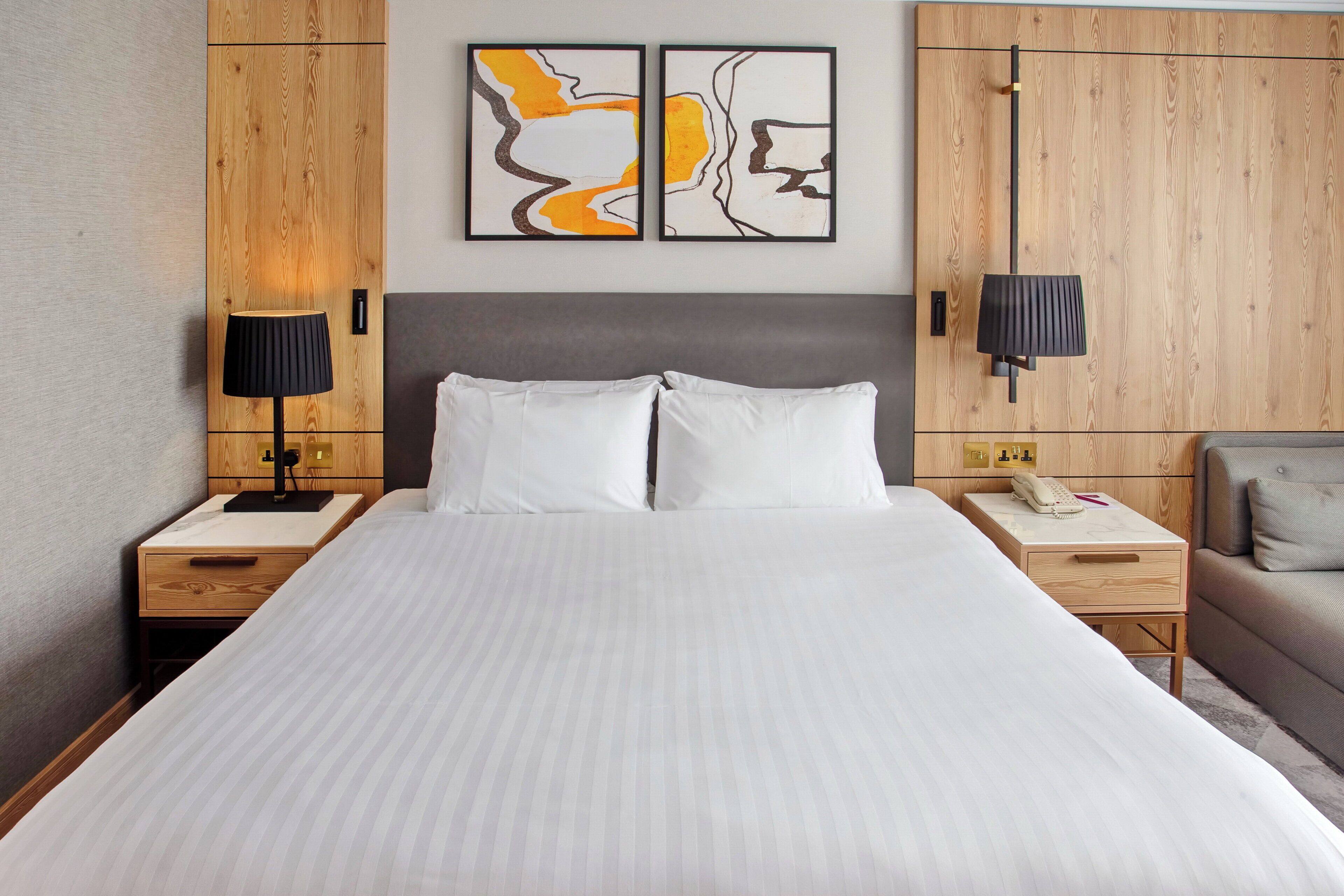 A hotel room with a large bed, two bedside tables, a nightstand, a sofa, and a wall-mounted telephone.