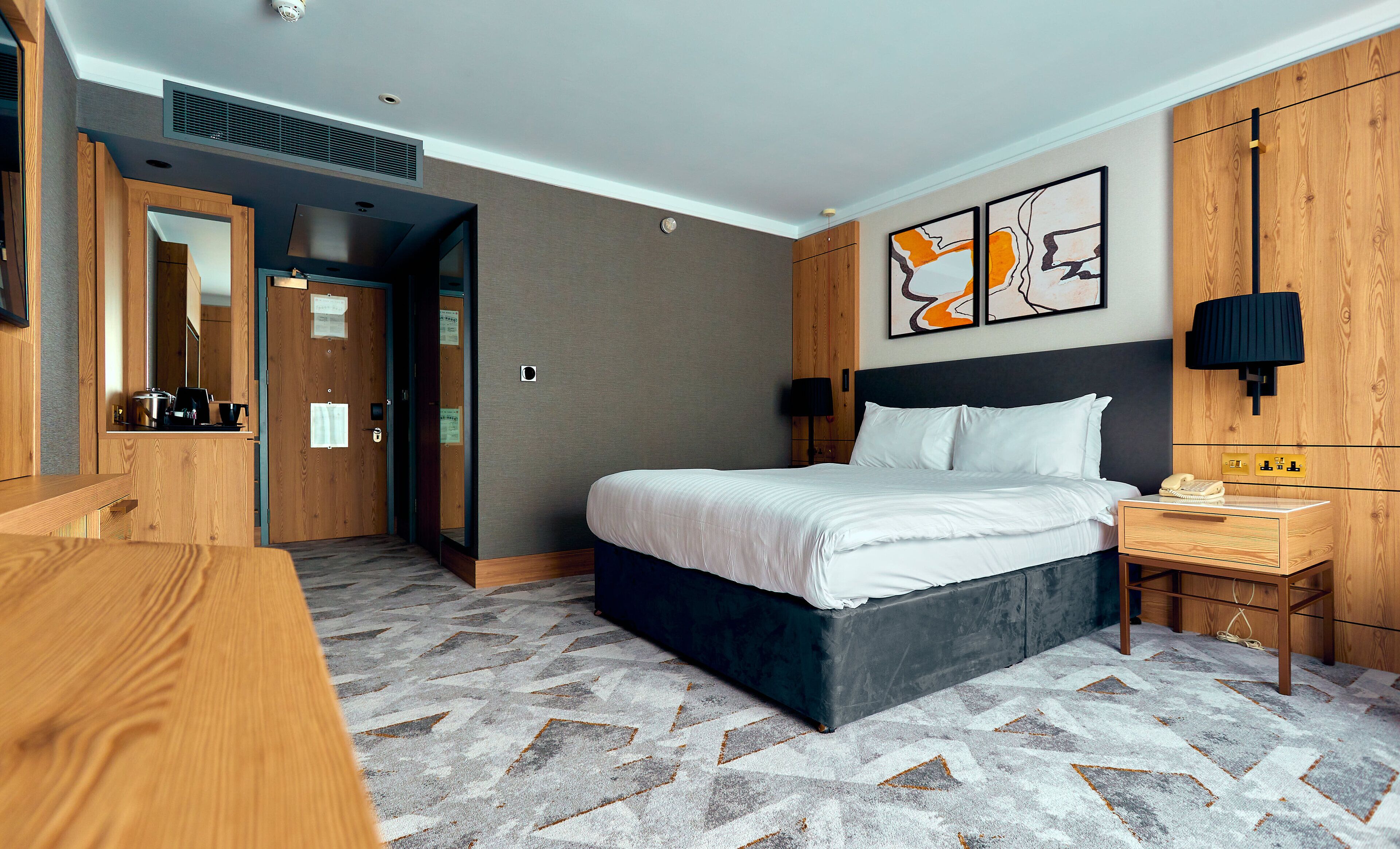 Una camera d'albergo con un letto, un comodino, una lampada e un armadio in legno.