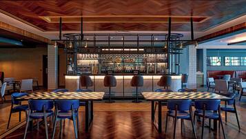 Zona de bar con suelo de madera en patrón de espiga, taburetes y una variedad de botellas y vasos.