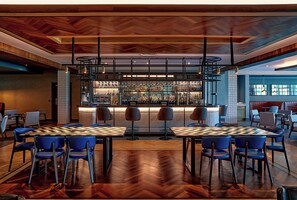 Zona de bar con suelo de madera en patrón de espiga, taburetes y una variedad de botellas y vasos.