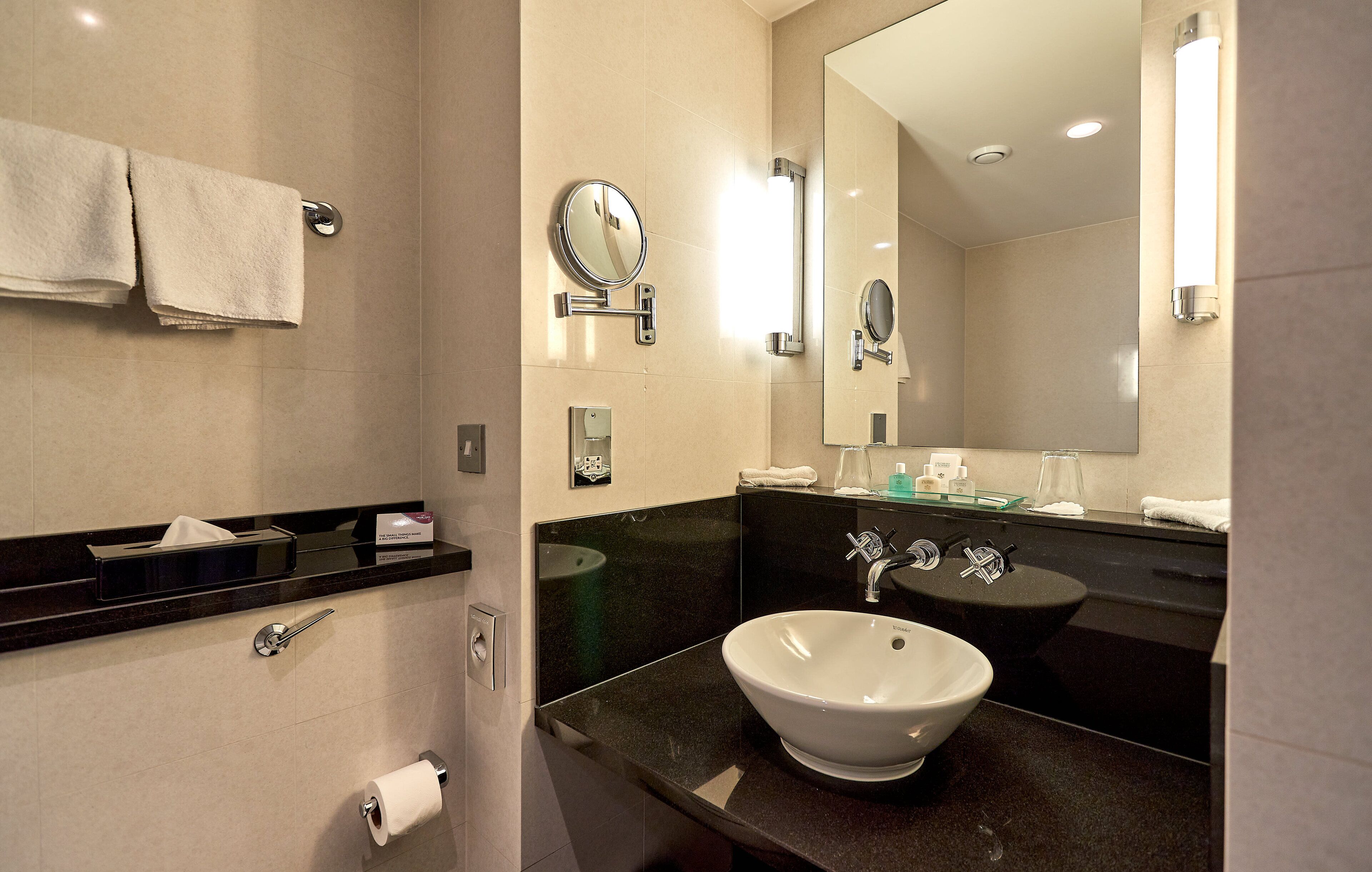 Une salle de bain moderne avec un plan de toilette noir, un lavabo blanc, un miroir et un porte-serviettes.