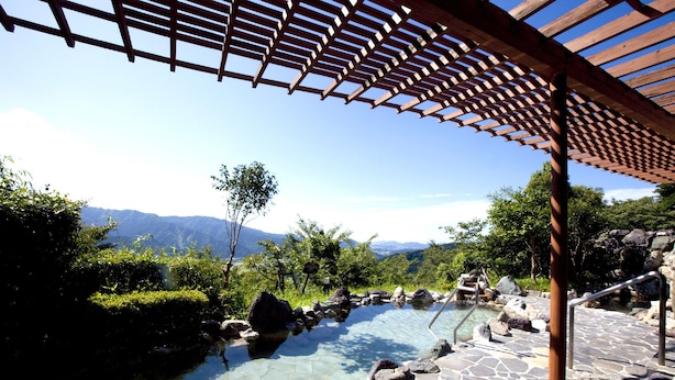 Ein Steingarten mit einem hölzernen Pergola, umgeben von Grünpflanzen und Bergen im Hintergrund.
