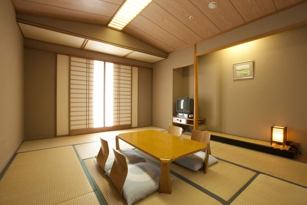 Une pièce de style japonais traditionnel, avec un sol recouvert de tatamis, une petite table en bois et un téléviseur.