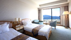 Ein Hotelzimmer mit zwei Betten, einem Schreibtisch, einem Sessel und einem Balkon mit Blick.