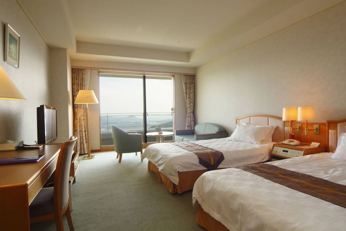 Une chambre d’hôtel avec deux lits, un bureau avec un ordinateur, une chaise, une petite table et une vue sur l’extérieur.