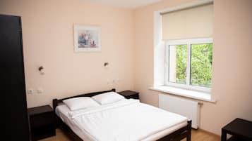 A bedroom with a bed, a window with a view, a nightstand, and a wall-mounted light.