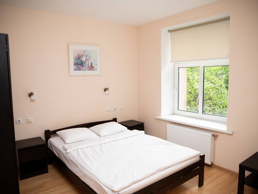 A bedroom with a bed, a window with a view, a nightstand, and a wall-mounted light.