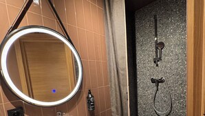 A bathroom with a sink, mirror, shower, and towel rack. - Hotel Avitar (Riga)