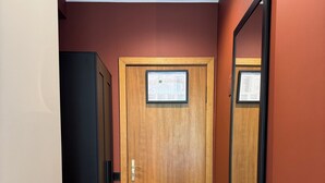 A hallway with a wooden door, a black cabinet, and a large mirror on the wall. - Hotel Avitar (Riga)