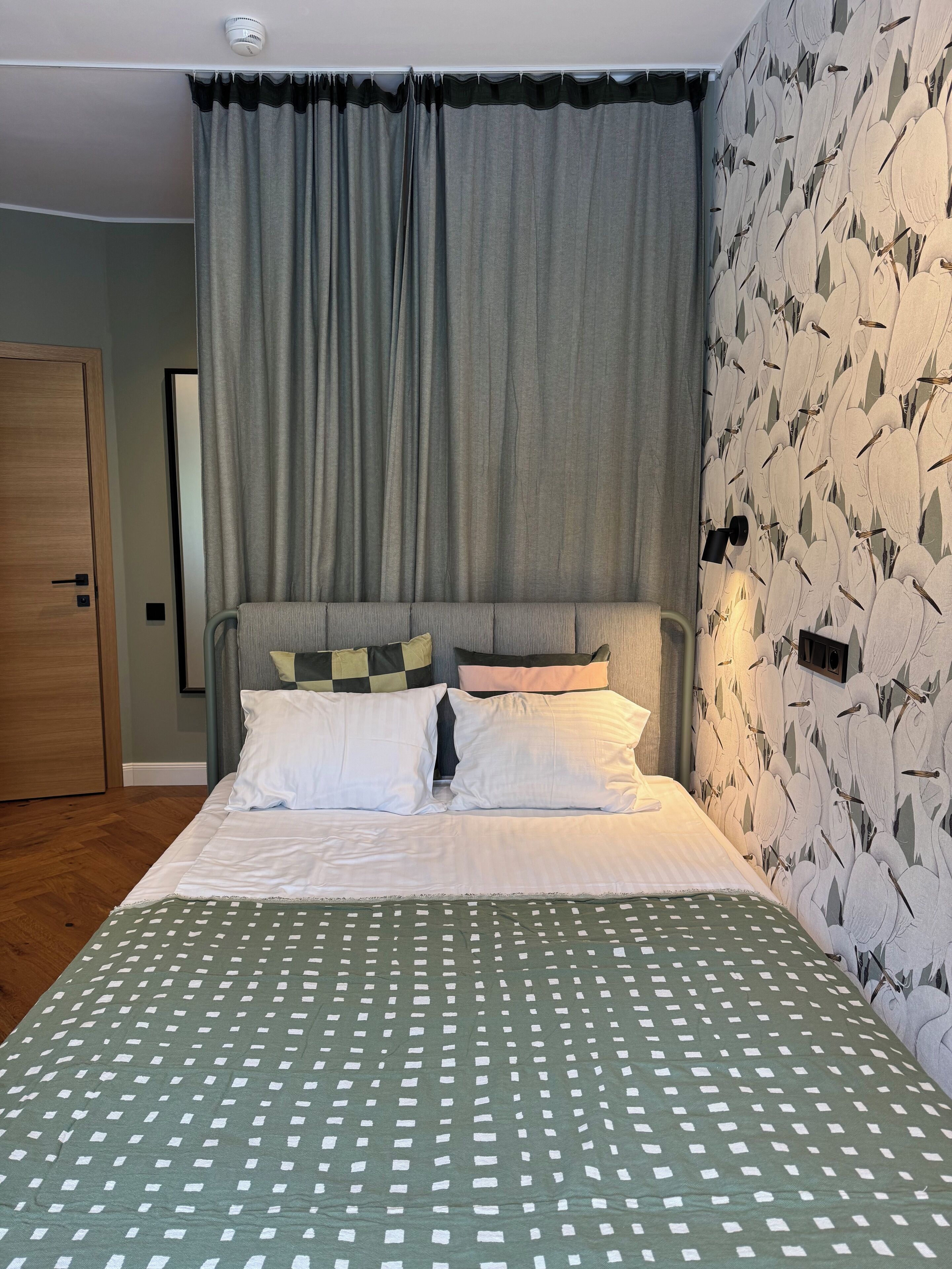 Une chambre à coucher avec un lit, des rideaux gris, un mur à motifs et une porte en bois.