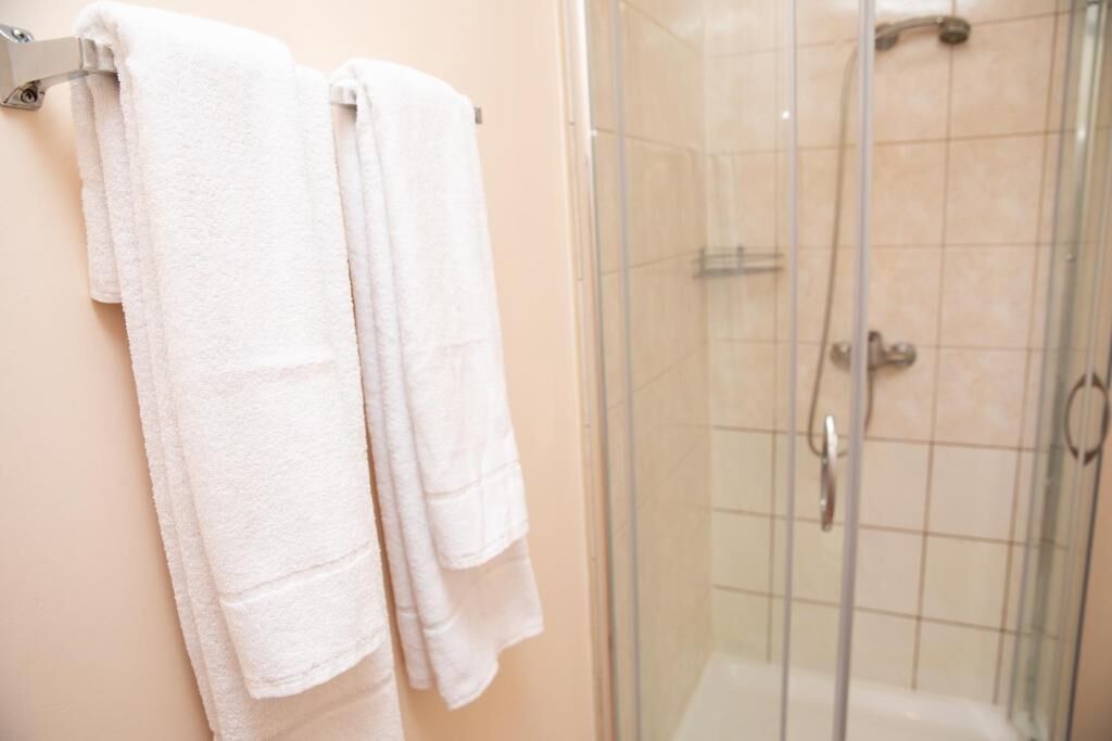 A bathroom with two white towels hanging on a rack, a glass shower enclosure, and a tiled wall.