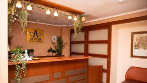 A hotel reception desk with a wooden counter, hanging plants, a clock, and a framed map on the wall. - Hotel Avitar (Riga)