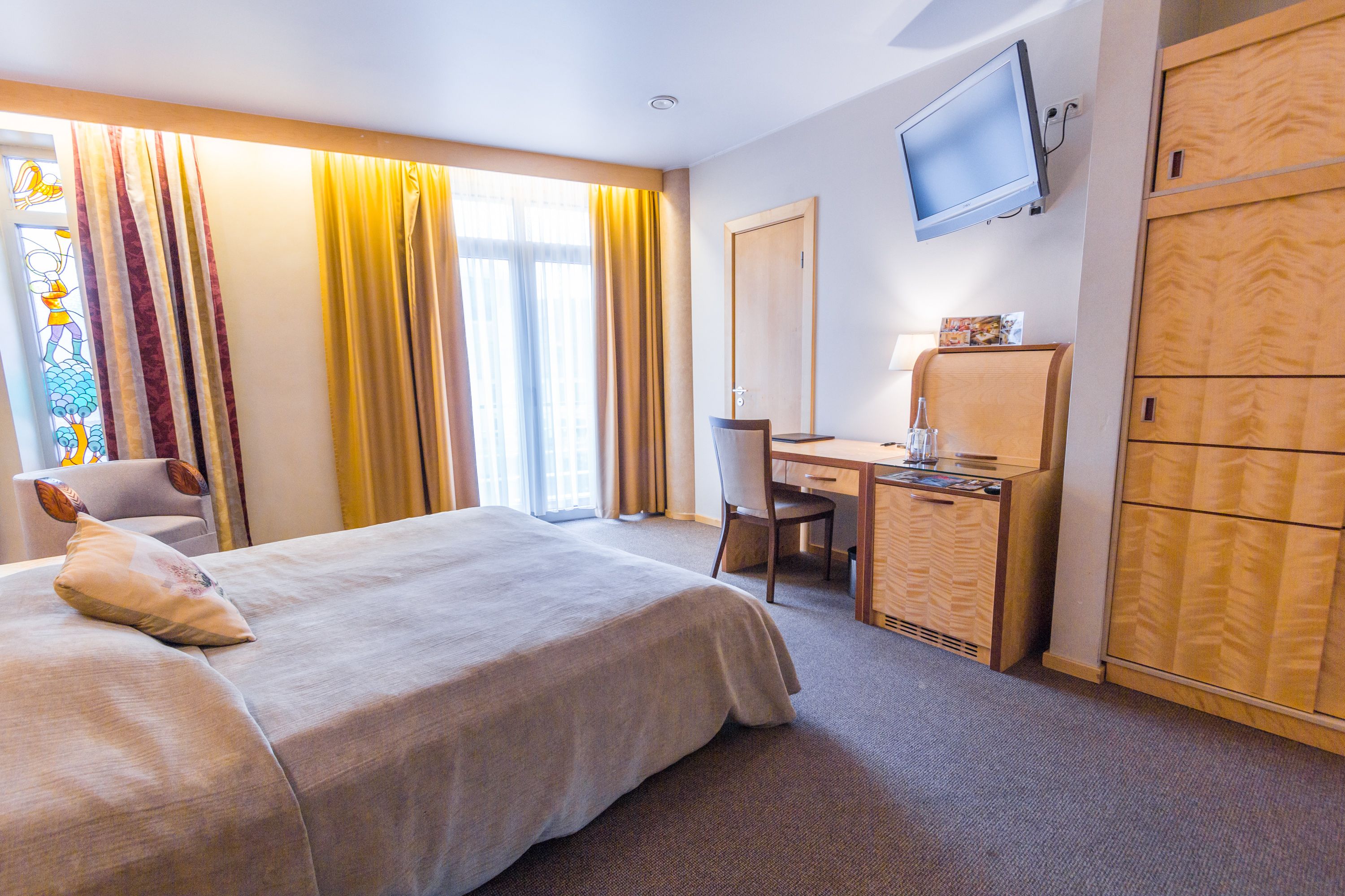 Ein Hotelzimmer mit Bett, Schreibtisch, Stuhl, Fernseher und Kleiderschrank.