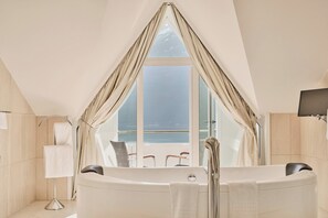 A modern bathroom with a freestanding bathtub, a large window with curtains, a towel rack, and a flat-screen TV. - Hotel Ullensvang (906914) (Lofthus)