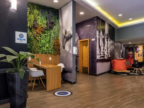 Una zona de recepció amb un taulell de fusta, cadires blanques, una paret verda amb plantes i una zona de descans amb seients taronja.