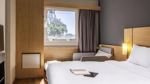 A hotel room with a large bed, a bedside table, a window with curtains, and a view of trees.