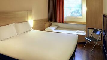 Quarto de hotel com uma cama grande, uma cama menor, uma mesa com cadeira, uma janela com cortinas e uma televisão.