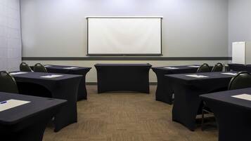A conference room with a projector screen, tables, chairs, and a refrigerator.