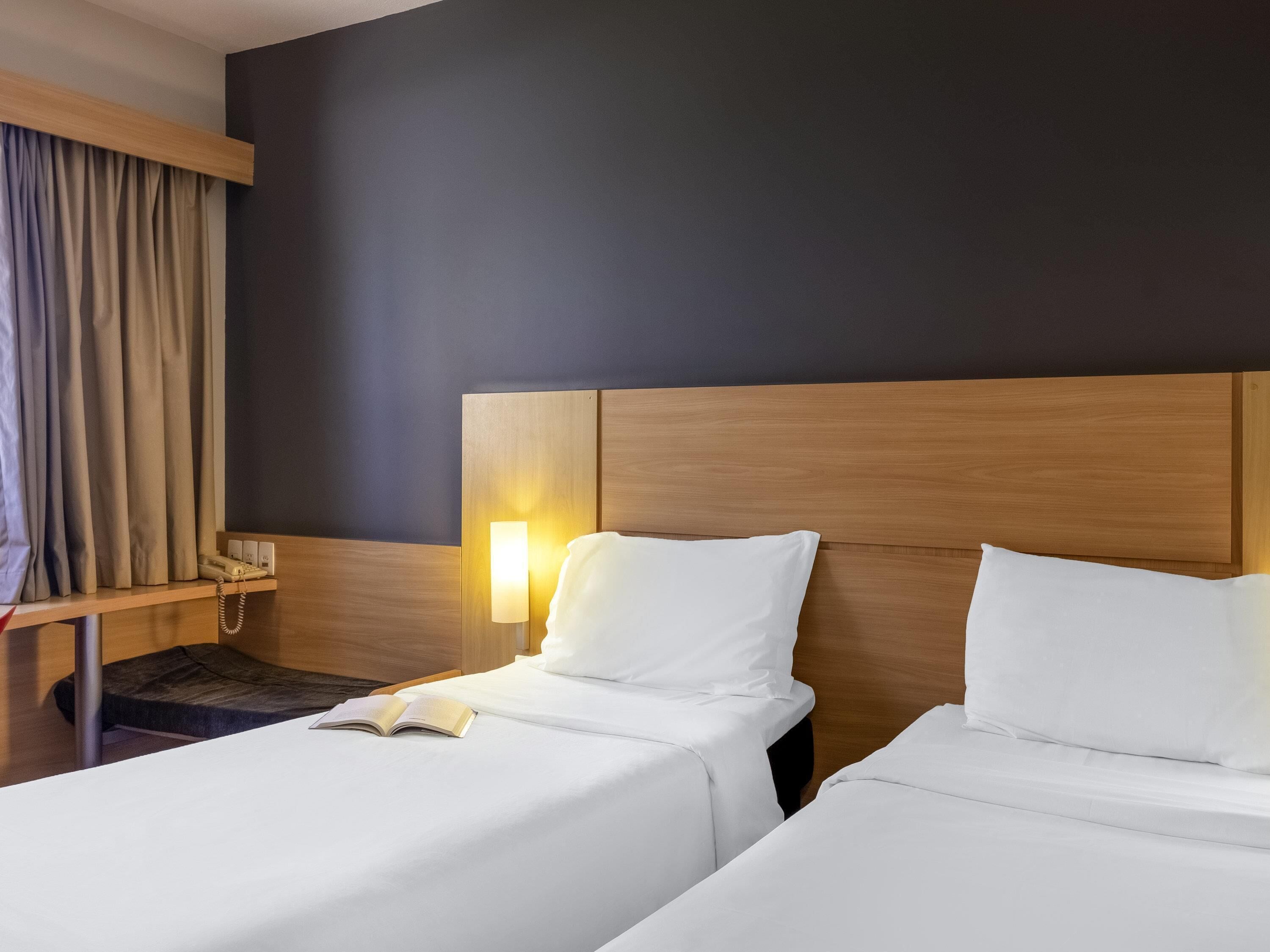 A hotel room with two beds, a bedside table with a lamp, and a telephone.