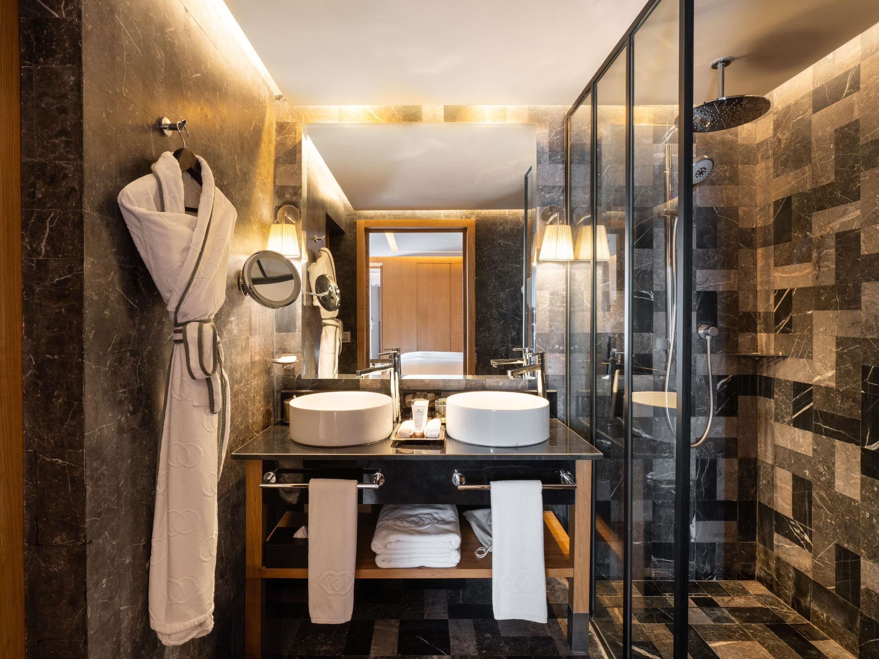 A modern bathroom with two sinks, a glass shower enclosure, and a robe hanging on a rack.