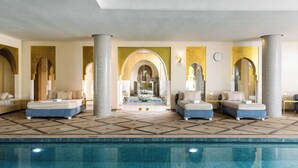 Un espace piscine intérieur luxueux, comprenant deux lits et une fontaine centrale.