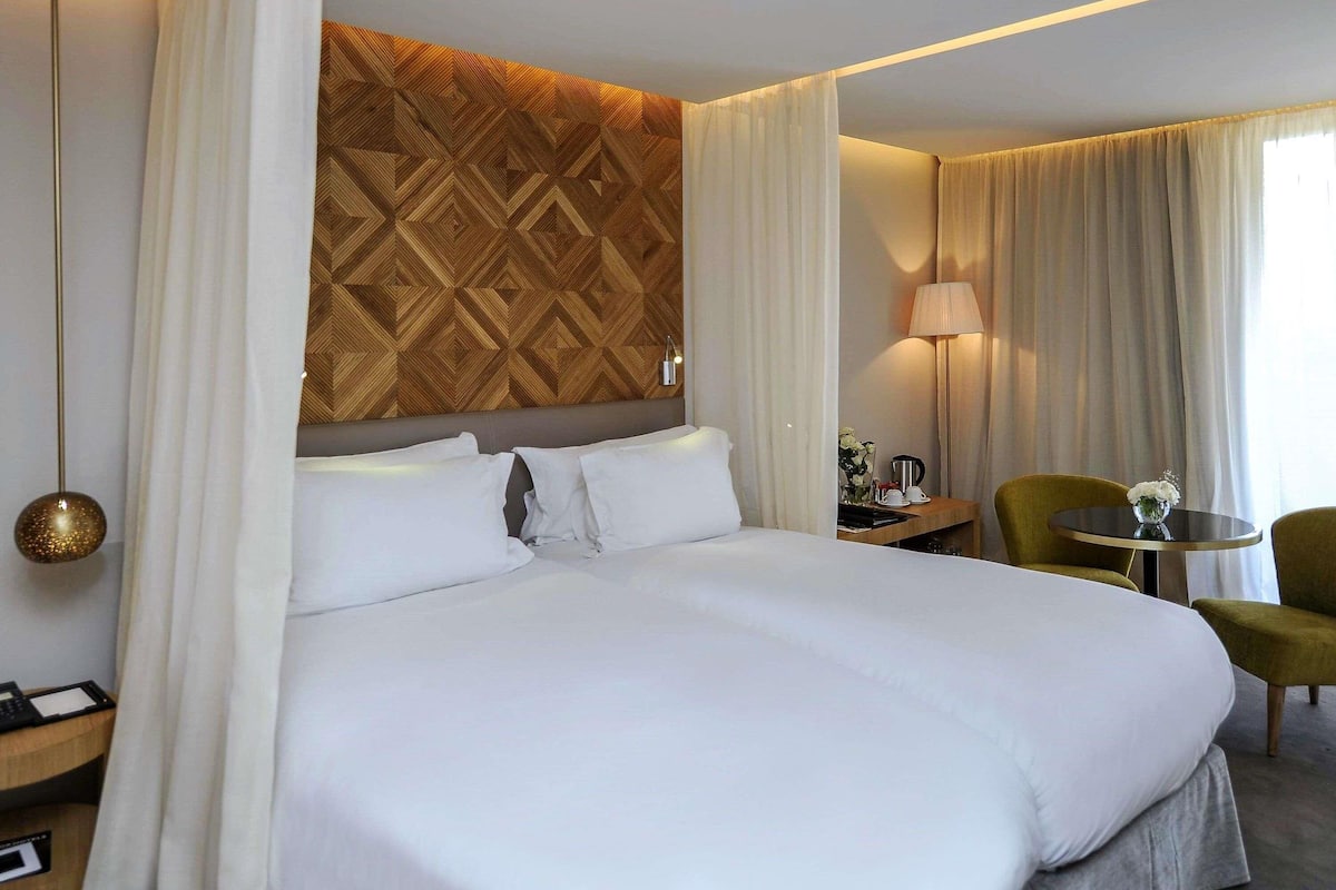 A hotel room with a large bed, a wooden accent wall, a desk with a lamp, and a chair.