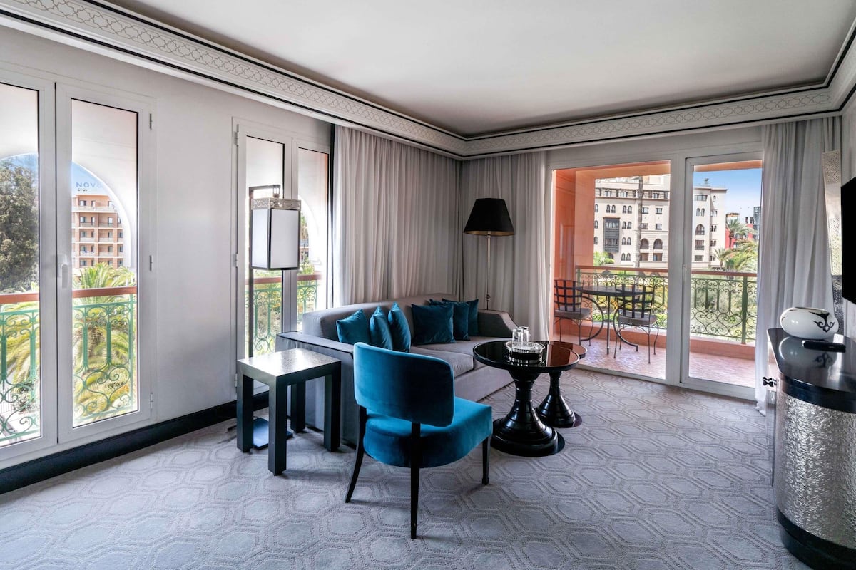 A modern hotel room with a balcony, a sofa, a dining table, and a TV.