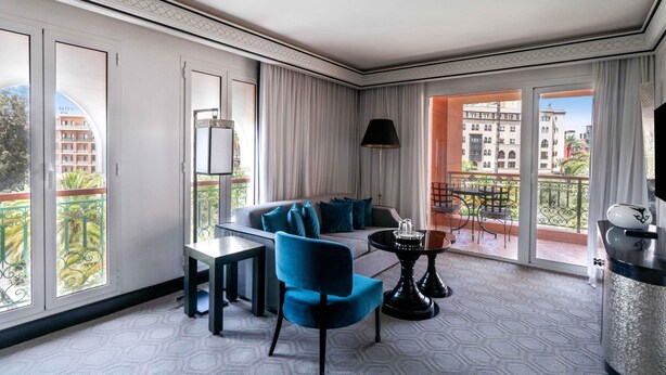 A modern hotel room with a balcony, a sofa, a dining table, and a TV.