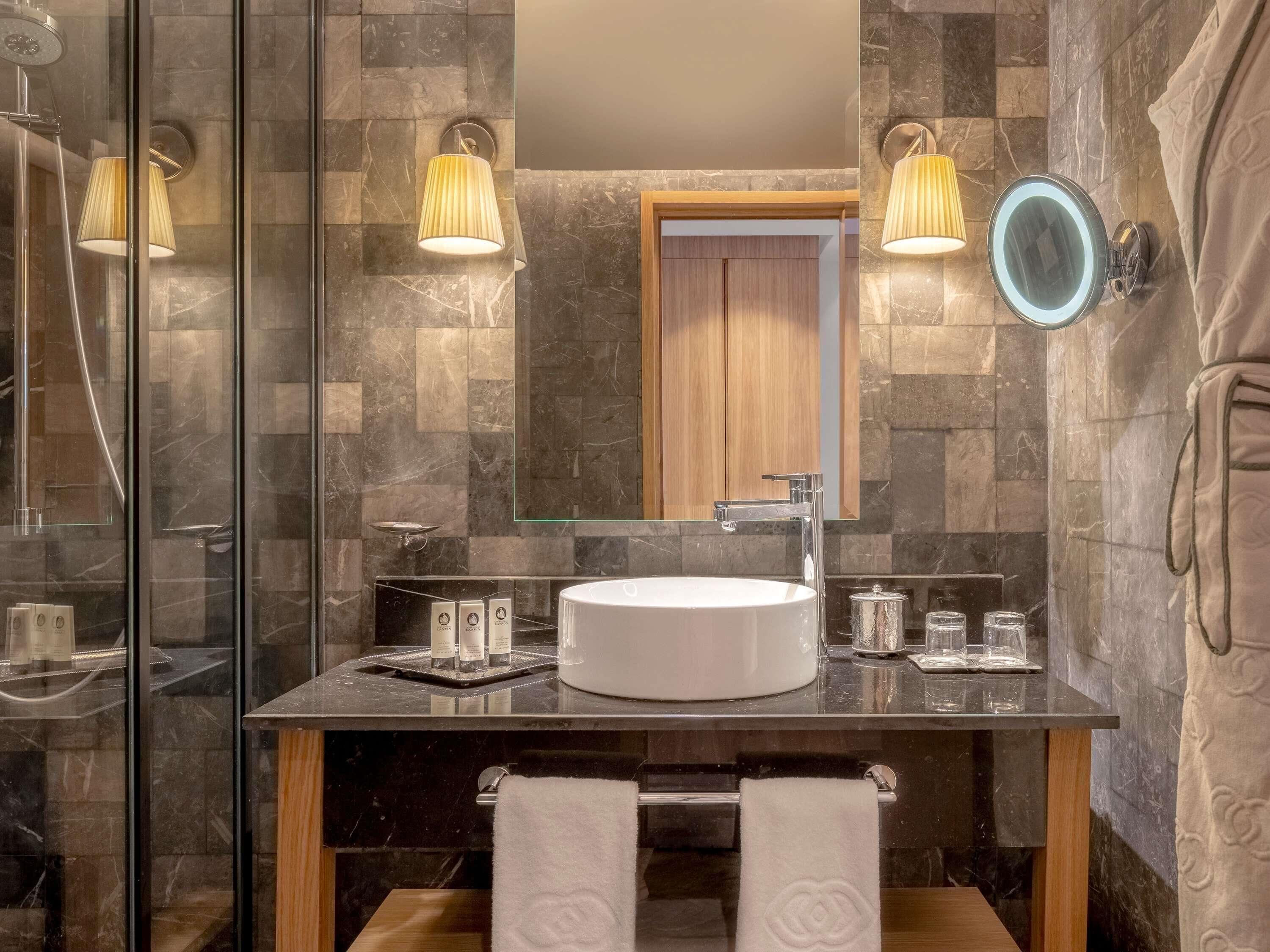 A modern bathroom with a glass shower enclosure, a round sink, and two wall-mounted lamps.