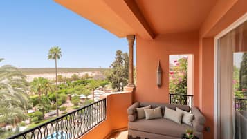 A balcony with a sofa, a table, and a view of a pool and greenery.