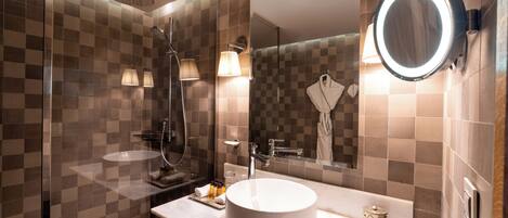 A modern bathroom with a round sink, a glass shower enclosure, and a mirror with a light.