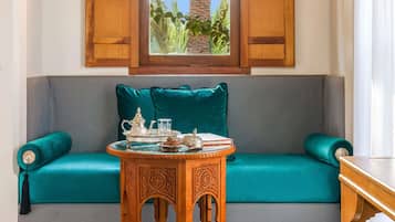 Un sofá color turquesa con vistas a palmeras a través de una ventana, una mesita de madera con una bandeja y un cojín decorativo.